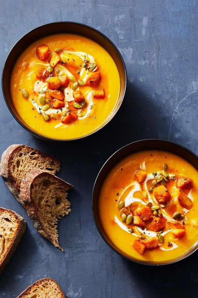 a bowl of squash soup next to a plate of bread