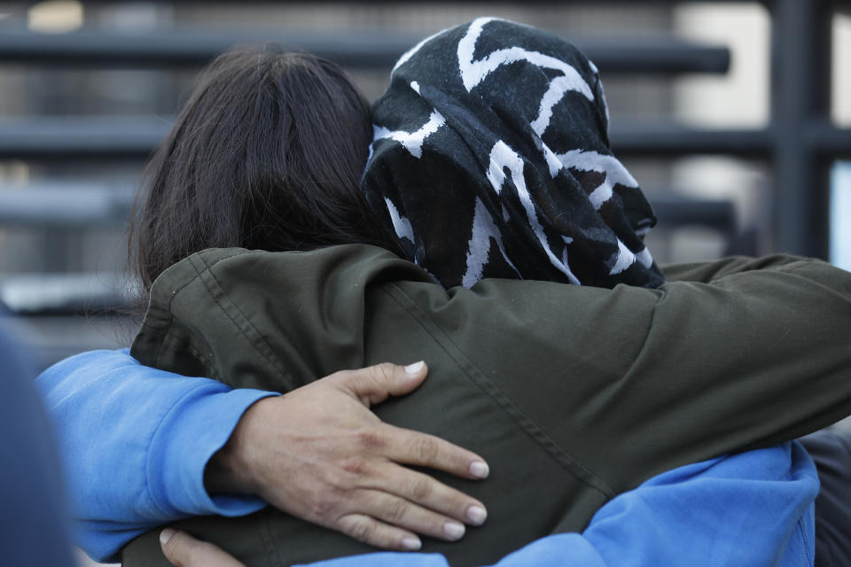 A Honduran asylum seeker, his face covered with a blanket, embraces an activist before entering the U.S. at San Diego's Otay Mesa port of entry, as seen from Tijuana, Mexico, Tuesday, Dec. 18, 2018. Six Honduran asylum seekers spent a chilly night camped out on a tiny patch of U.S. soil at a San Diego border crossing seeking to have their claims processed. (AP Photo/Moises Castillo)