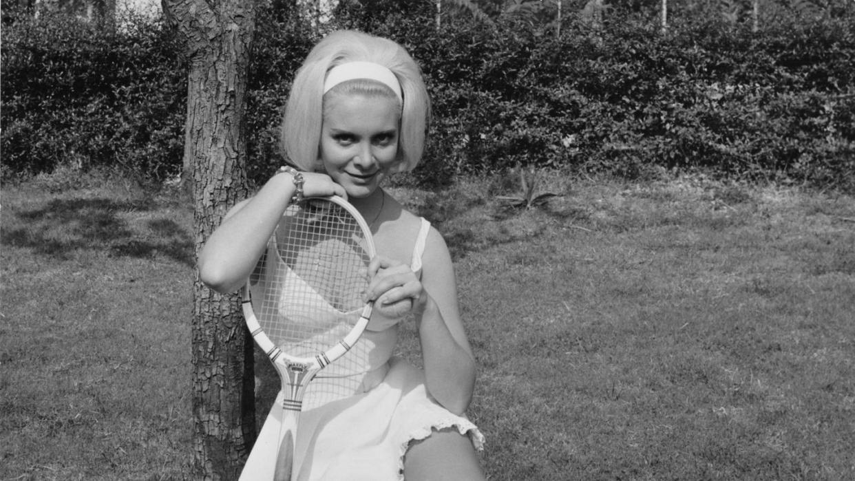 a little girl sitting on the grass holding a tennis racket