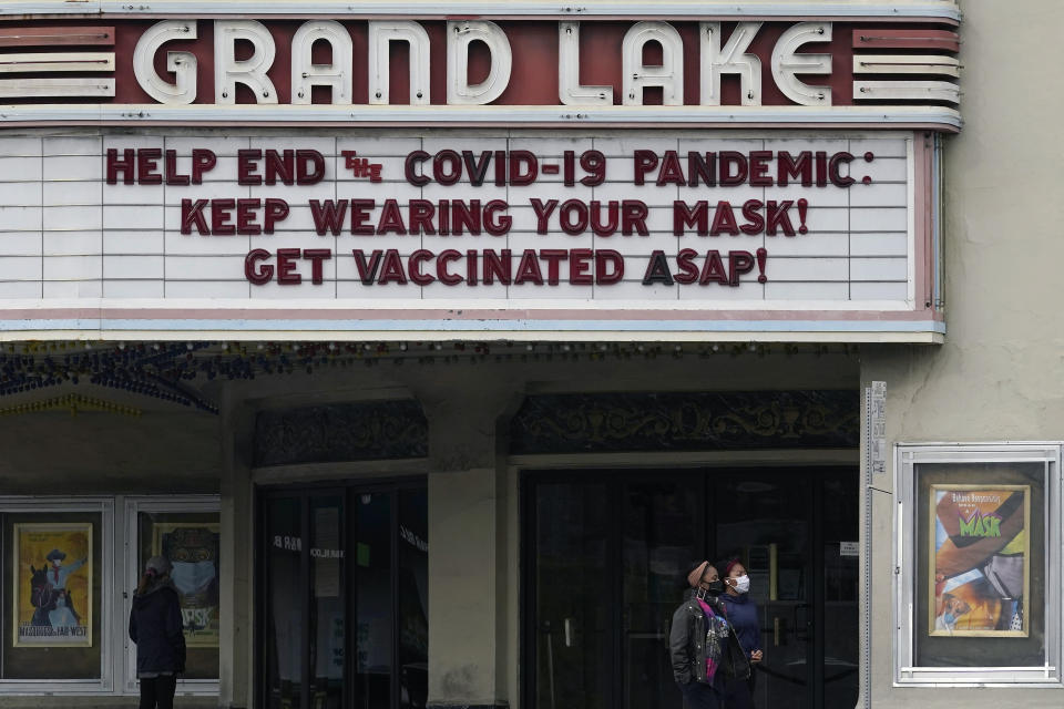 People walk below a sign on the marquee of the Grand Lake Theater advising people to wear masks and get vaccinated during the coronavirus pandemic in Oakland, Calif., Tuesday, March 9, 2021. (AP Photo/Jeff Chiu)