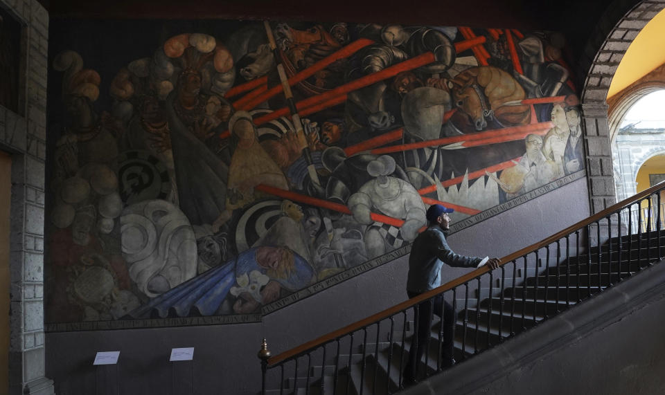 Historian Jonatan Chavez ascends a flight of stairs past a mural by Jean Charlot titled, “Massacre en el Templo Mayor”, illustrating the 1521 massacre that the Spaniards led in the most sacred site of the Aztec empire, at the former Jesuit college Antiguo Colegio de San Ildefonso in Mexico City, Wednesday, April 26, 2023. (AP Photo/Marco Ugarte)