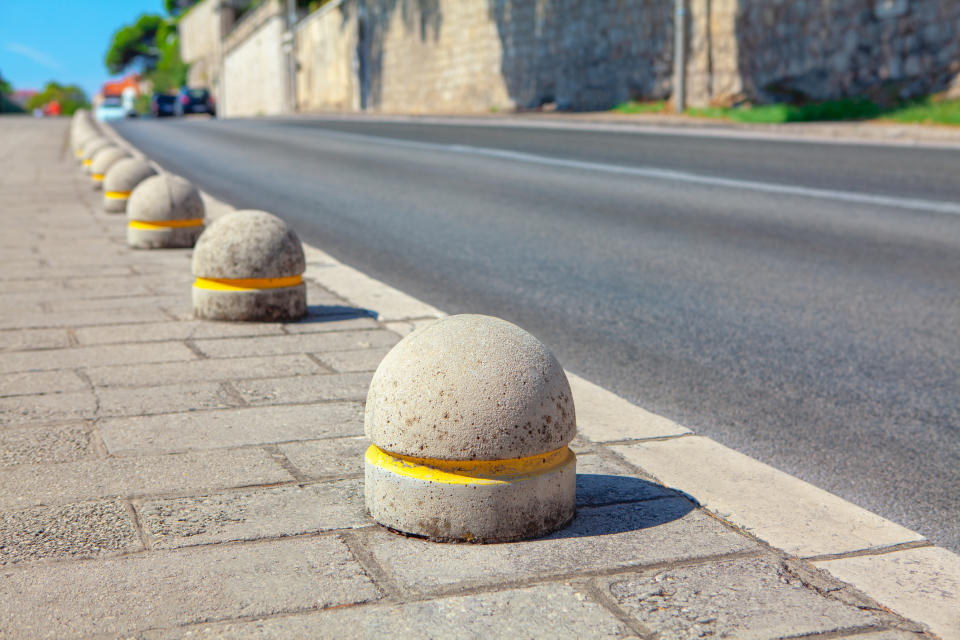 Concrete bollards with yellow stripes line a sidewalk next to an empty street