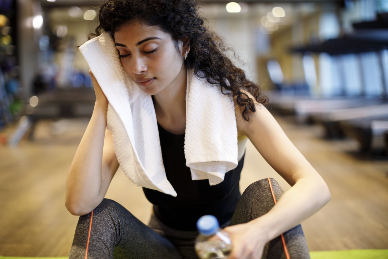 woman sweating at gym wiping face with towel