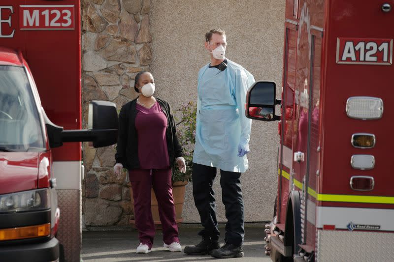 A nursing home worker and a medic talk while others transport a patient to an ambulance at the Life Care Center of Kirkland, the long-term care facility linked to several confirmed coronavirus cases in the state, in Kirkland