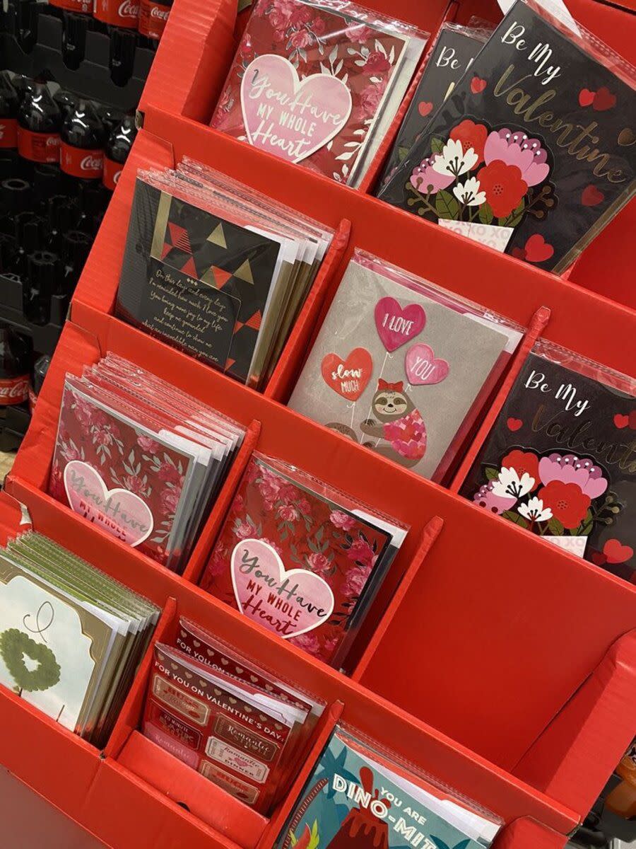 Four rows of Valentine's Day greeting cards in a red cardboard case at Aldi, Monrovia, California, diagonal, bottles of Coke in the top left in the background