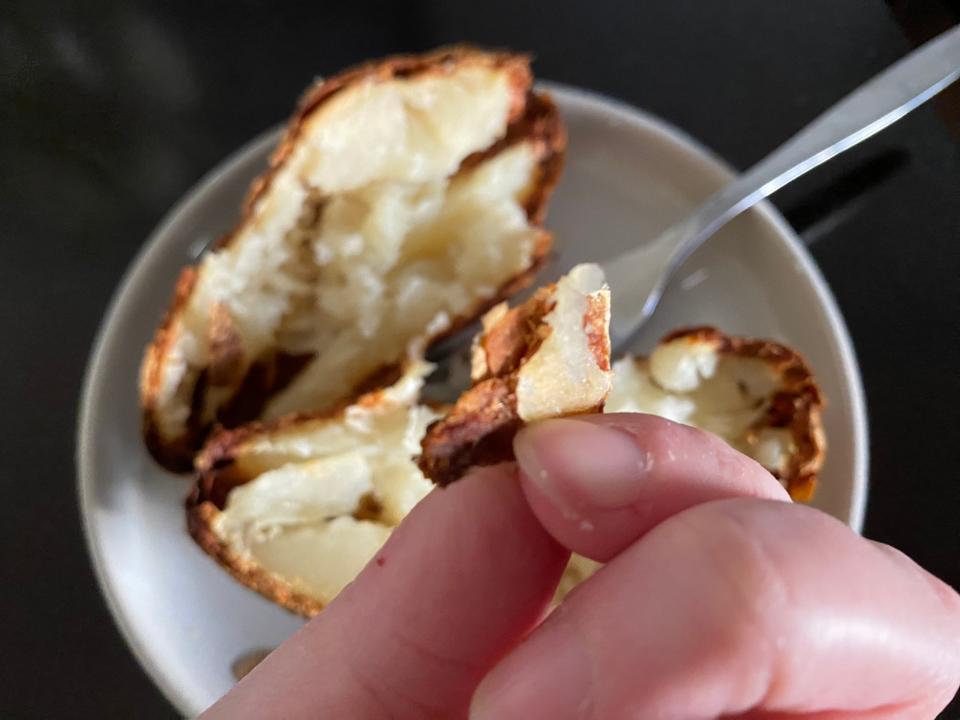 hand holding up crispy baked potato skin over a baked potato on a plate
