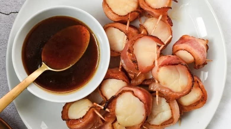 Top-down view of bacon wrapped scallops on a plate with a sauce dish