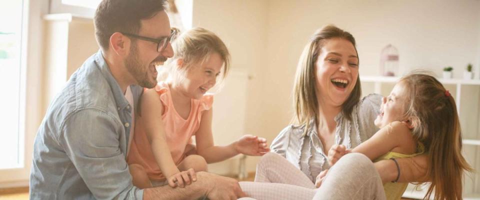 Happy family with two daughters playing at home. Family sitting on floor and playing together.