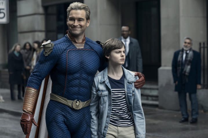 Homelander holds a boy's shoulder as he walks down the street.