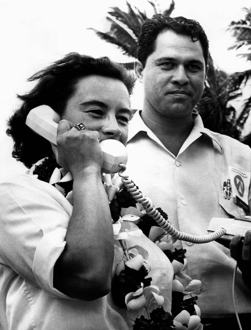 FILE - This photo made April 13. 1964, in Honolulu, Hawaii, shows Jerrie Mock talking to her husband in Columbus, Ohio, during her solo flight around the world. Fifty years ago Mock became the first woman to fly solo around the world. With Mock is George Montgomery, a supervisor with the phone company who installed the phone. (AP Photo)