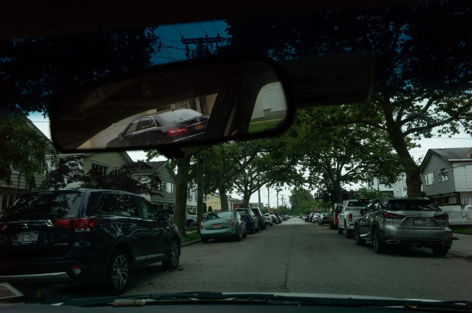 A tree-lined street is seen through the front window of a car.