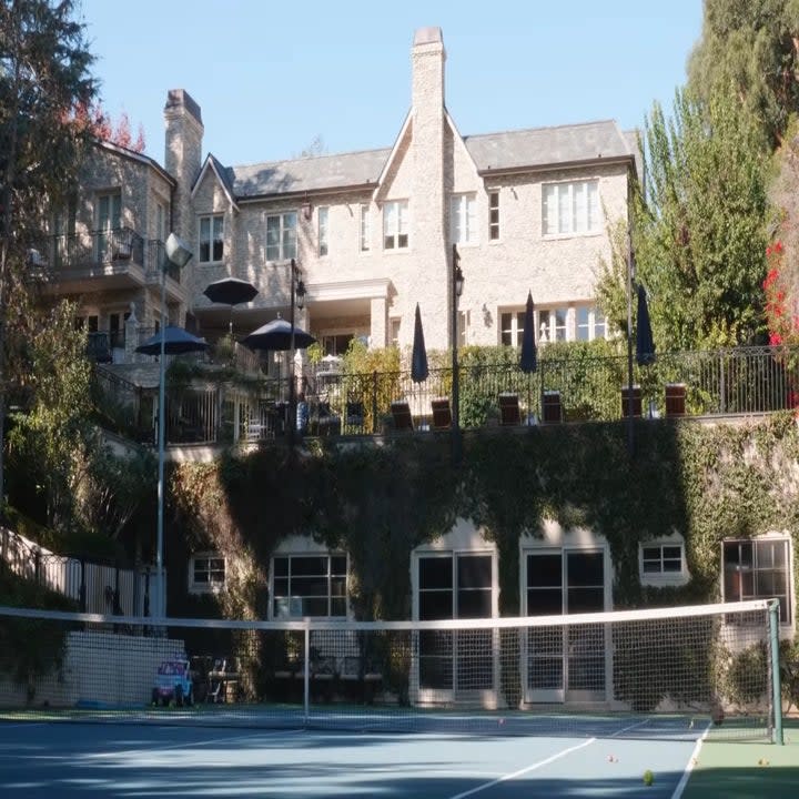 The backyard has a tennis court and the exterior has greenery on it