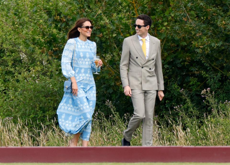 Kate Middleton in long blue dress walking with Lee Thompson in a grey suit and yellow tie.