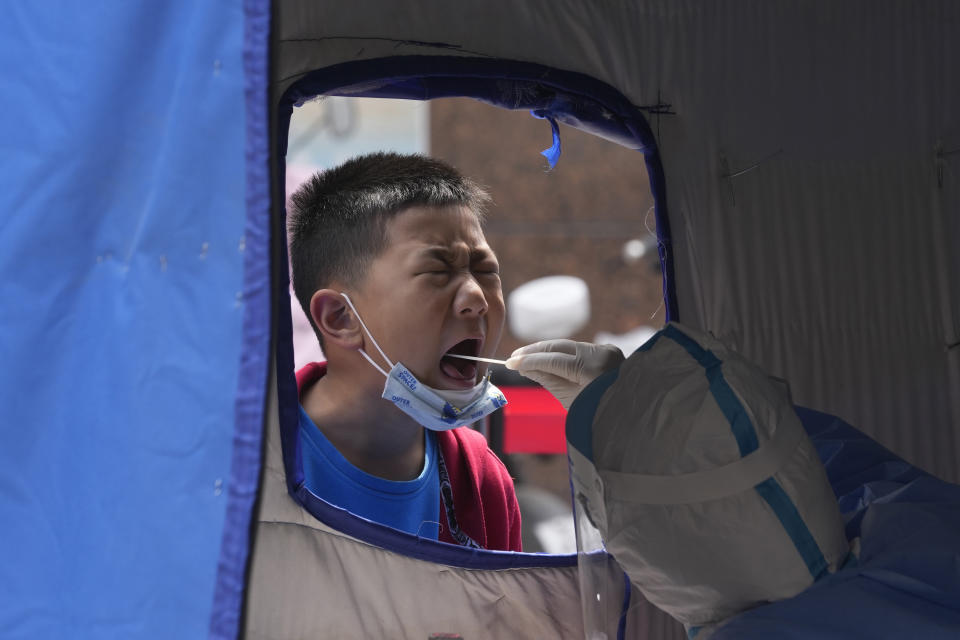 A child opens his mouth to be swabbed for mass COVID test on Thursday, May 12, 2022, in Beijing. China's leaders are struggling to reverse an economic slump without giving up anti-virus tactics that shut down Shanghai and other cities, adding to challenges for President Xi Jinping as he tries to extend his time in power. (AP Photo/Ng Han Guan)