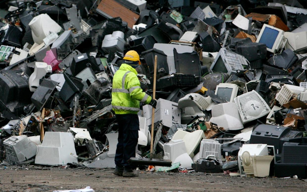 A workman clears debris from around a pile of old television sets and computer monitors awaiting processing at a recycling company in the UK.  - PA
