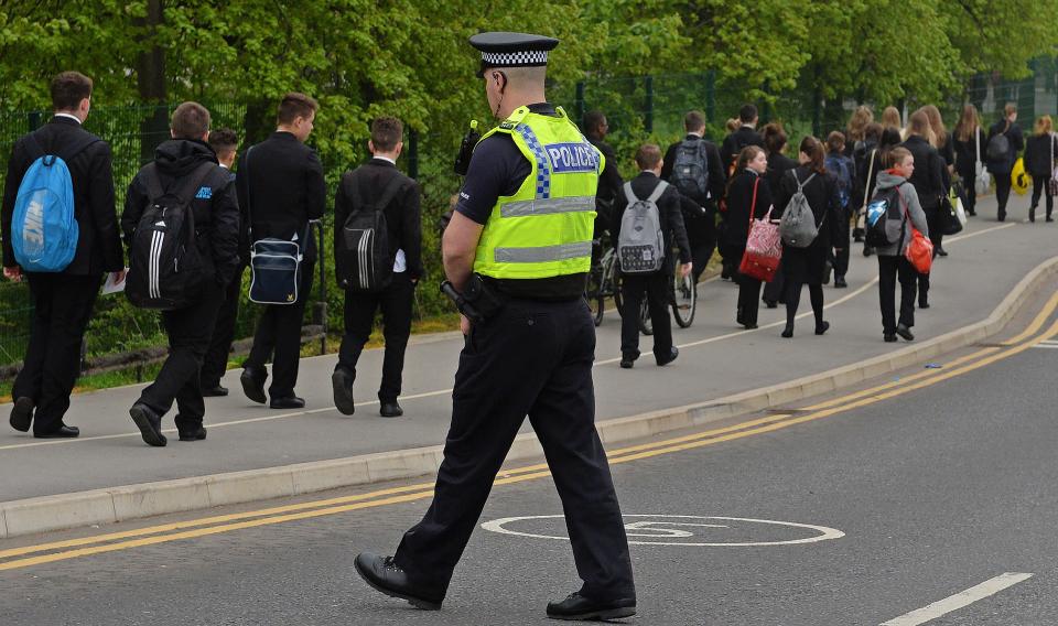 A police officer patrols as pupils (L) arrive for school at Corpus Christi Catholic College in Leeds, northern England on April 29, 2014, following the fatal stabbing of Spanish teacher Anne Maguire by a pupil Monday. Police arrested a 15-year-old male pupil after a female teacher was stabbed to death at a Catholic school in Britain on Monday. AFP PHOTO / PAUL ELLIS        (Photo credit should read PAUL ELLIS/AFP via Getty Images)