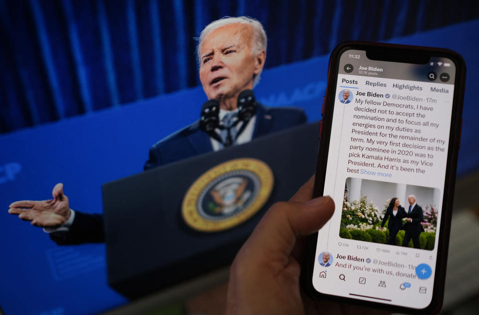 In a photo illustration, a hand in the foreground holds up a phone showing President Biden's announcement on social media. A photo of Biden is visible in the background.