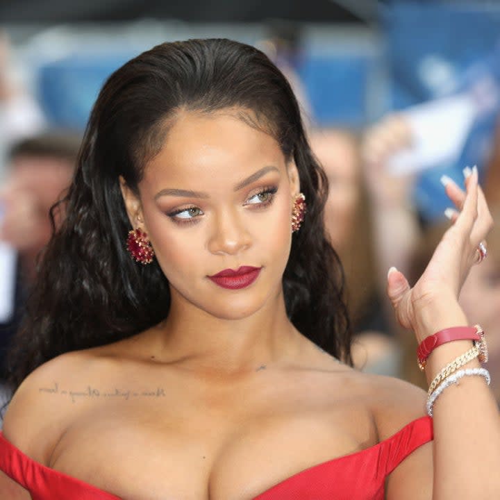 Headshot of Rihanna looking off to her left, her hair is slicked back and she rocks a red sleeveless dress and matching lipstick and earrings