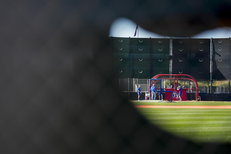 Texas Rangers players take batting practice, seen through a hole in the outfield tarps, during spring training baseball workouts Wednesday, Feb. 14, 2024, in Surprise, Ariz. (AP Photo/Lindsey Wasson)