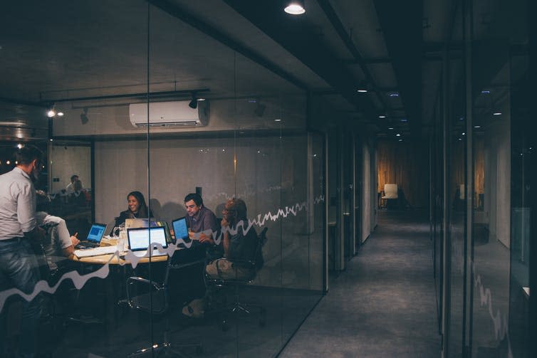 A group of work colleagues sitting in a late night meeting in a dark office.