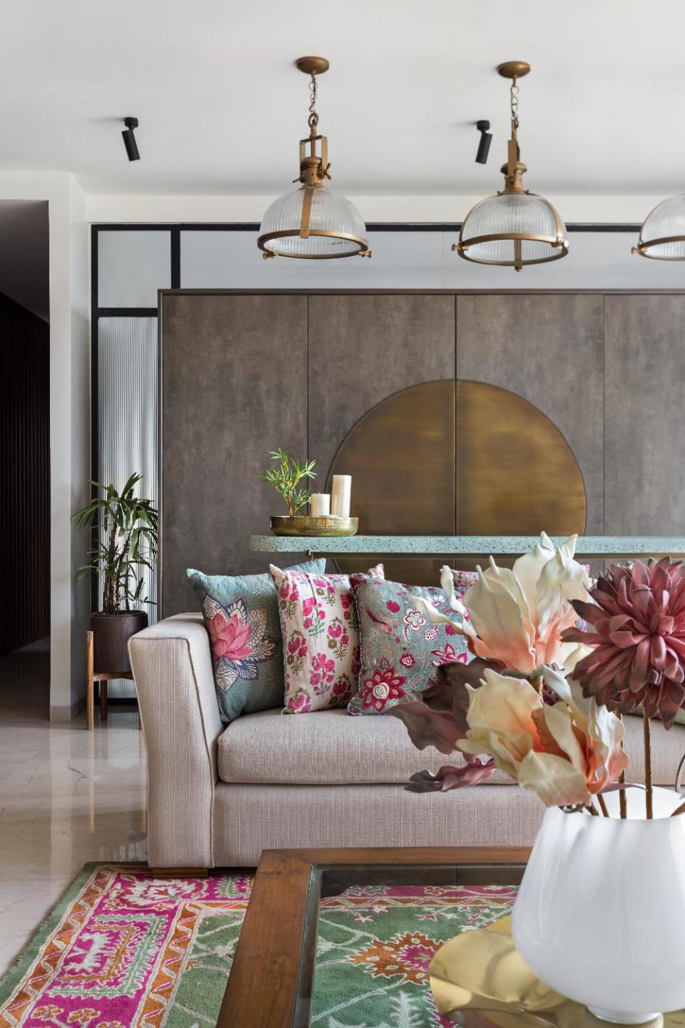 A stone and brass bar unit serves as a minimalist backdrop that anchors the expansive living cum dining room. Bass echoes in the detailing of the pendant lamps, the legs of the bar table and the centerpiece on the coffee table. Pendant lamp by <a href="https://fave.co/2QvqrQb" rel="noopener" target="_blank" data-ylk="slk:Gulmohar Lane;elm:context_link;itc:0;sec:content-canvas" class="link ">Gulmohar Lane</a>; sofa by <a href="https://fave.co/2qg4zh0" rel="noopener" target="_blank" data-ylk="slk:Cottons and Satins;elm:context_link;itc:0;sec:content-canvas" class="link ">Cottons and Satins</a>; throw cushions by <a href="https://fave.co/37jLJG8" rel="noopener" target="_blank" data-ylk="slk:Good Earth;elm:context_link;itc:0;sec:content-canvas" class="link ">Good Earth</a>; carpet by <a href="https://fave.co/2Om0UpK" rel="noopener" target="_blank" data-ylk="slk:Humming Haus;elm:context_link;itc:0;sec:content-canvas" class="link ">Humming Haus</a>.