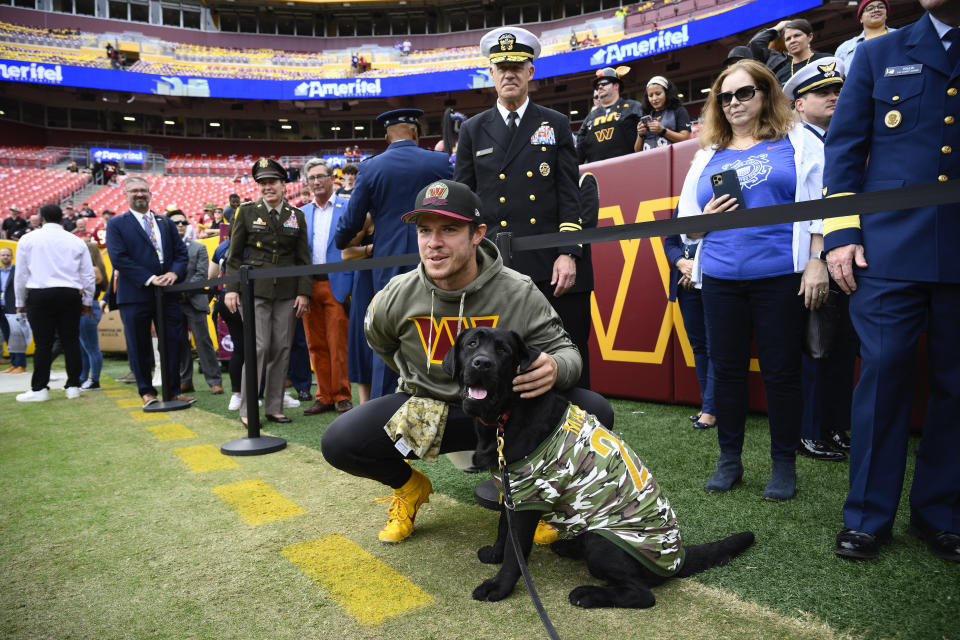 Washington Commanders quarterback Taylor Heinicke (4) poses with a dog as he meets fans and members of the military before the start of an NFL football game against the Minnesota Vikings, Sunday, Nov. 6, 2022, in Landover, Md. (AP Photo/Nick Wass)