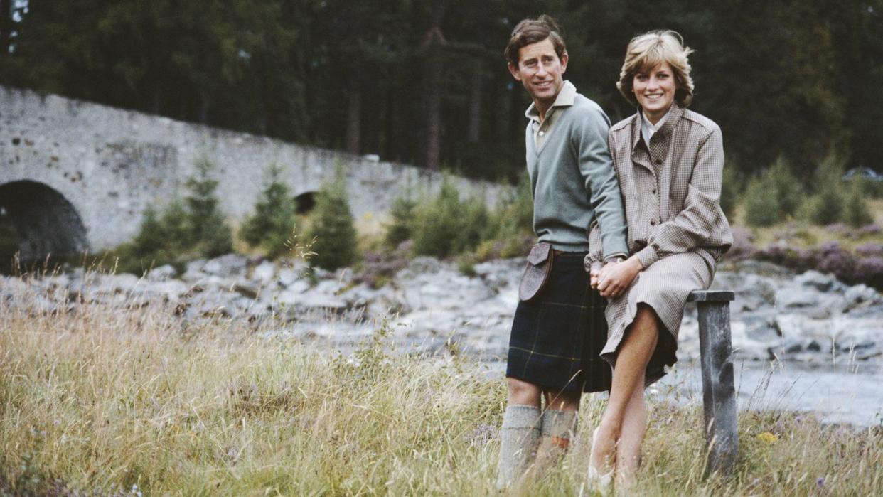 prince charles and princess diana stand in a field near a river and hold hands, both smile