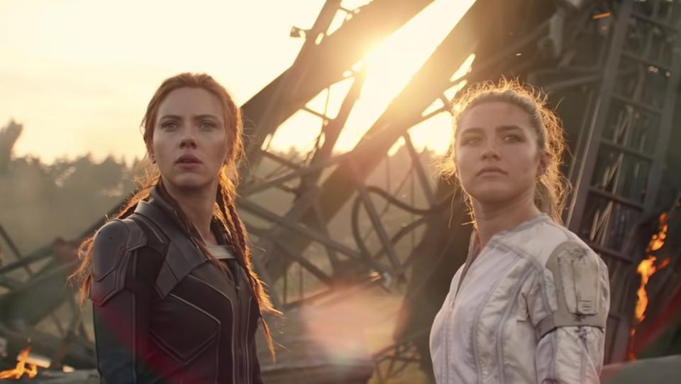 Natasha Romanoff and Yelena Belova stand before fiery wreckage in a moment from Black Widow.