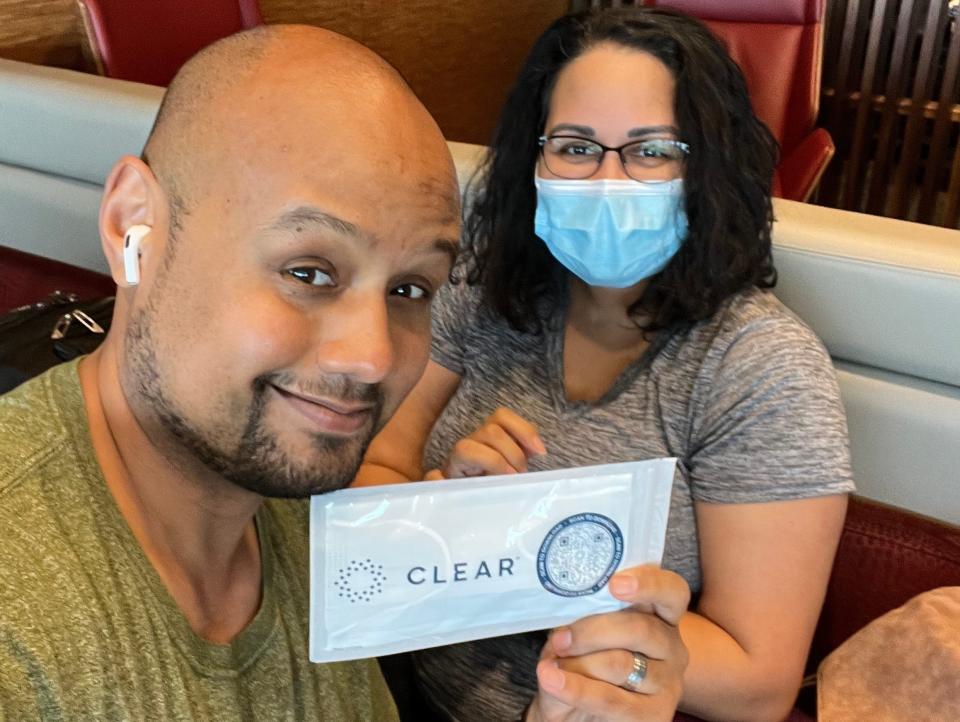 A man and a woman taking a picture holding up a sign for the airport service, Clear.