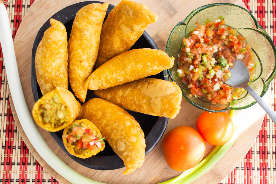 A plate of empanadas with one open cut, along with a bowl of salsa and fresh tomatoes
