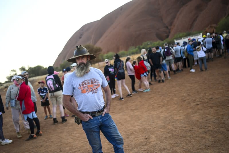 A man wearing a T-shirt saying "I chose not to climb" stands next to tourists lining up to climb Uluru, formerly known as Ayers Rock, at Uluru-Kata Tjuta National Park in the Northern Territory