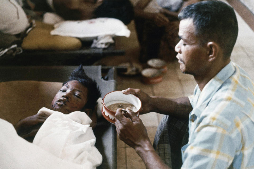 FILE - In this in February 1974, file photo, a Cambodian father kneels at the side of his son, blinded in both eyes, during the Khmer Rouge rocket and artillery shelling of Phnom Penh, Cambodia. The last surviving leaders of the communist Khmer Rouge regime that brutally ruled Cambodia in the 1970s were convicted of genocide, crimes against humanity and war crimes Friday, Nov. 16, 2018, by an international tribunal. (AP Photo/Carl D. Robinson, File)