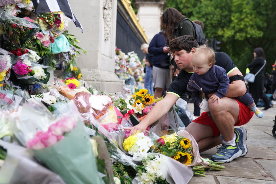 A man with a young child lays flowers outside Buckingham Palace, London, following the death of Queen Elizabeth II on Thursday. Picture date: Friday September 9, 2022.