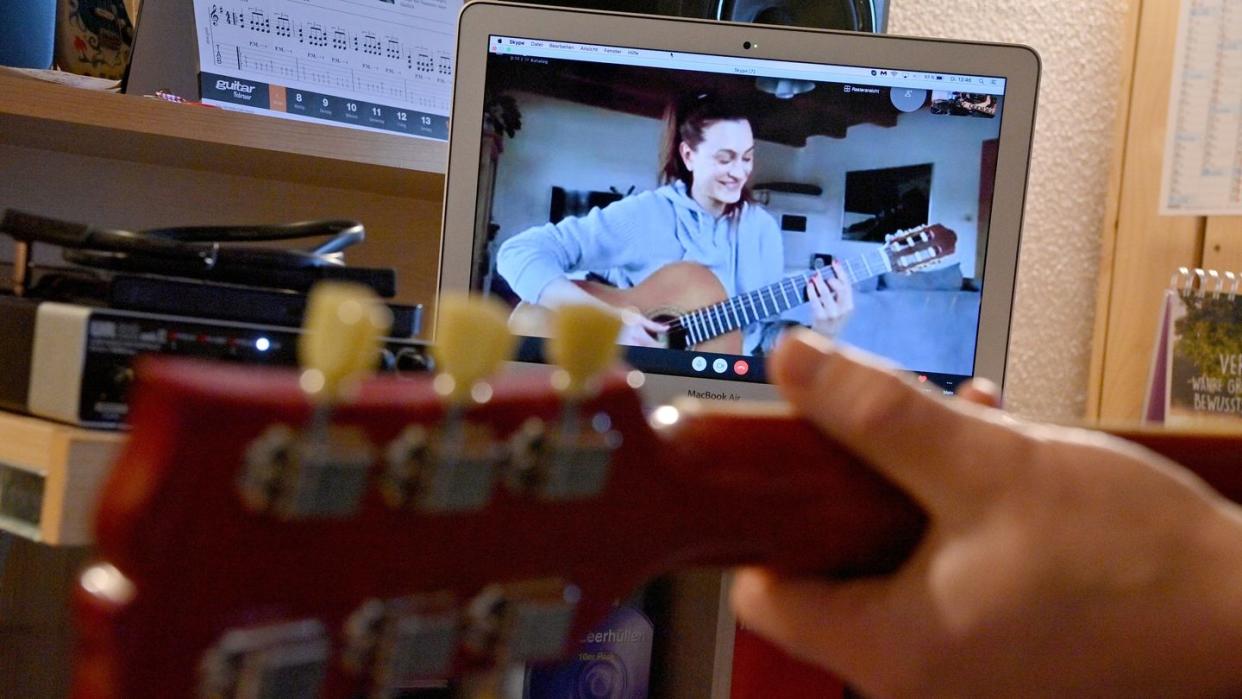 Ein Gitarrenlehrer unterrichtet eine Schülerin  via Online-Videokonferenz.