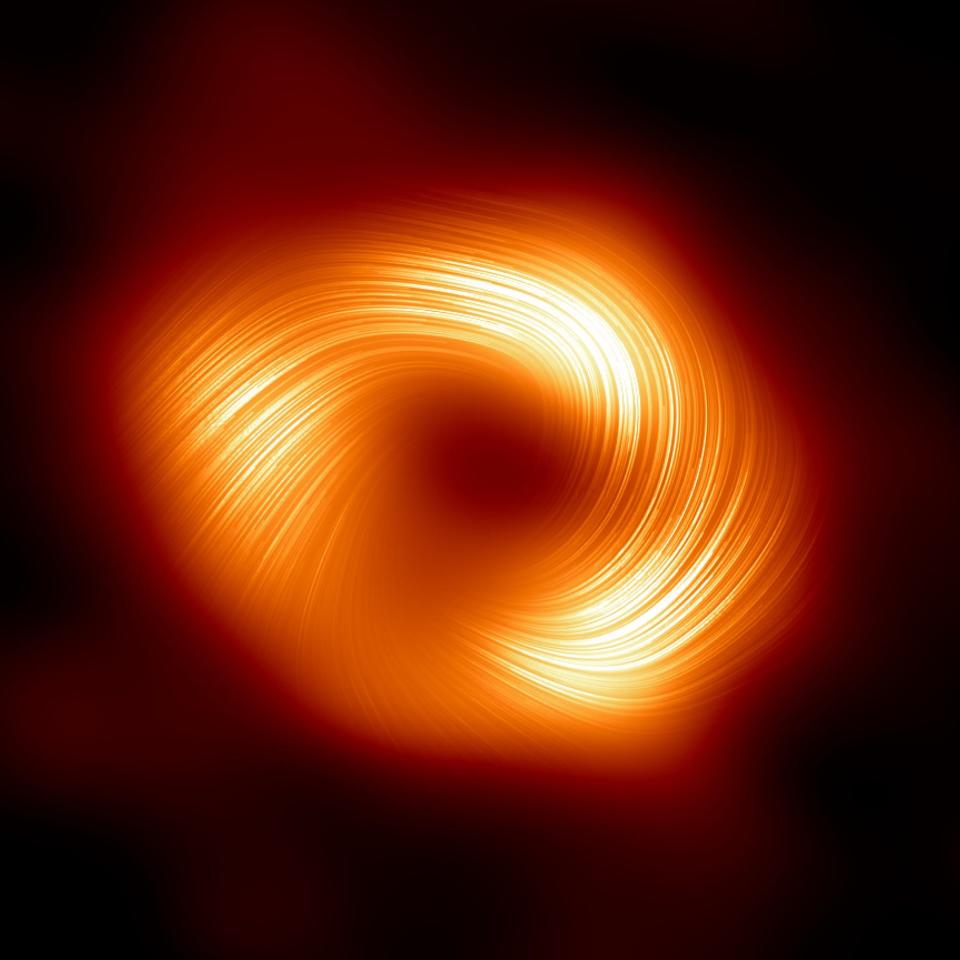 black hole polarization image shows a circle of bright yellow and diffuse orange light in the blackness of space with lines swirling in one direction along the circle and a black spot in the middle