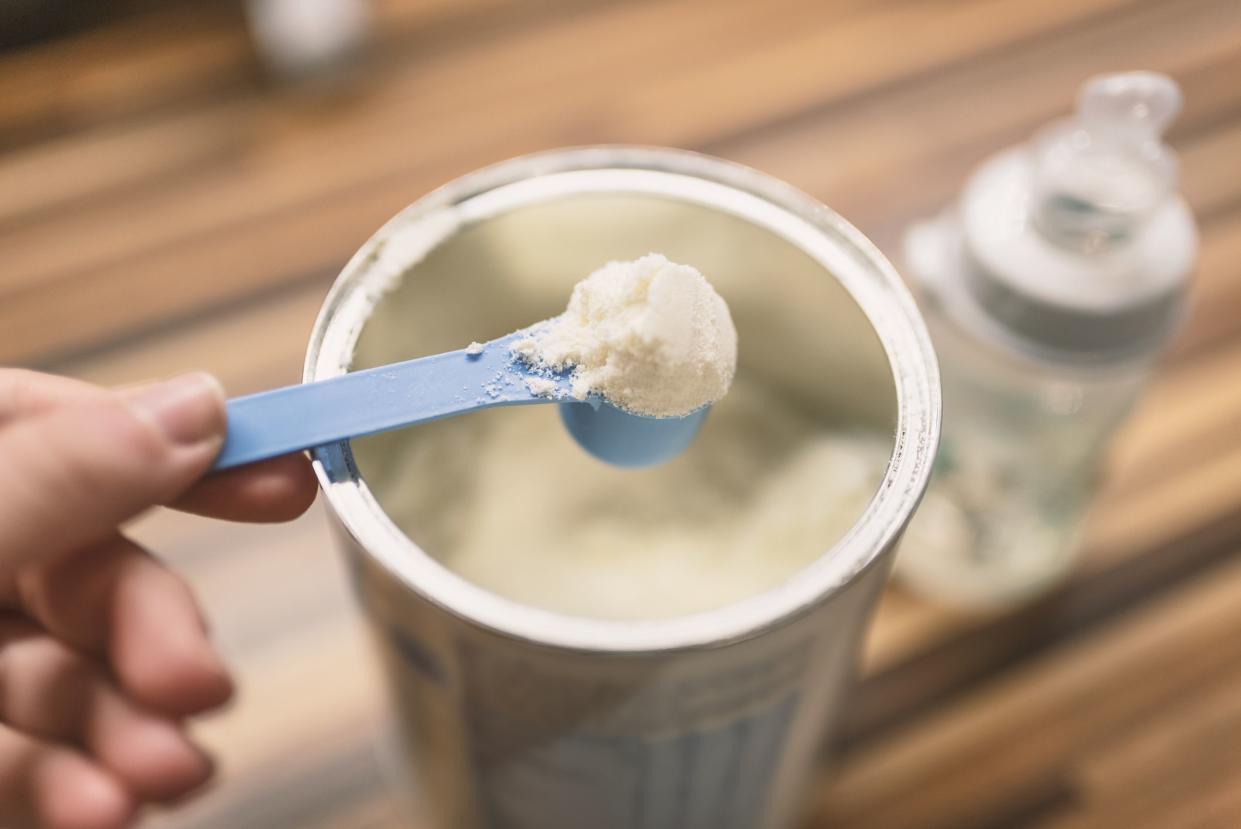 Powder milk for baby and blue spoon on light background close-up. Milk powder for baby in measuring spoon on can. Powdered milk with spoon for baby. Baby Milk Formula and Baby Bottles. Baby milk formula on kitchen background