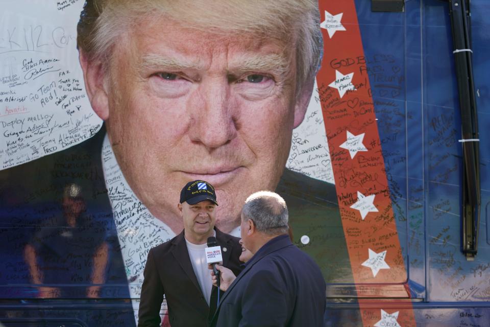 Pennsylvania GOP gubernatorial candidate Doug Mastriano and his wife Rebecca speak with talk show host John Fredericks next to Fredericks' bus with an image of former President Donald Trump before the start of a campaign event Nov. 7.