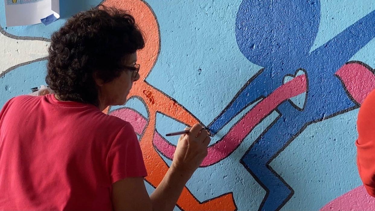 A volunteer paints a portion of the L.O.V.E. is the Answer mural, located at the corner of Moreau Street and South Delmorr Avenue in Morrisville.