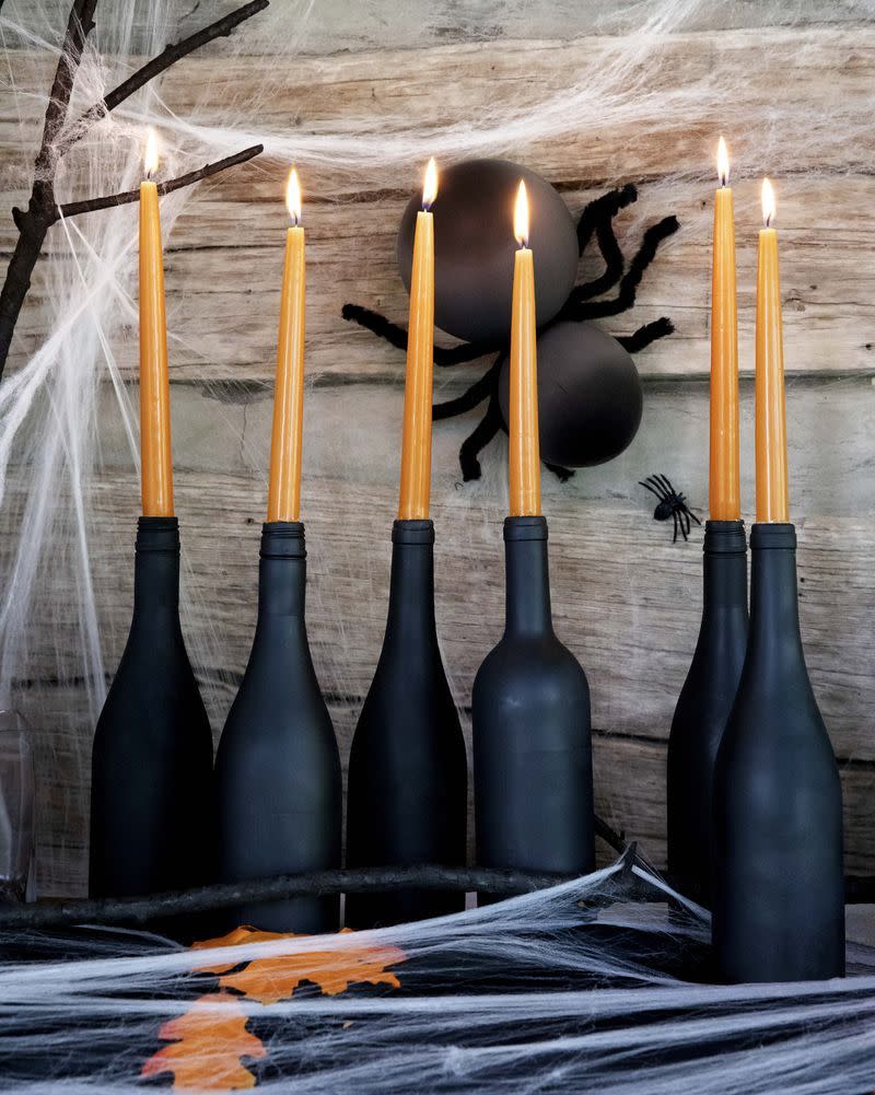 <p>An eerie flicker is a must for any Halloween mantel. Paint wine bottles with matte-black spray paint. Once dry, insert an orange taper candle in each. (Remember to keep candles away from anything flammable, and never burn unattended.) The spider is crafted with balloons, wire, and black faux fur—so clever!</p>