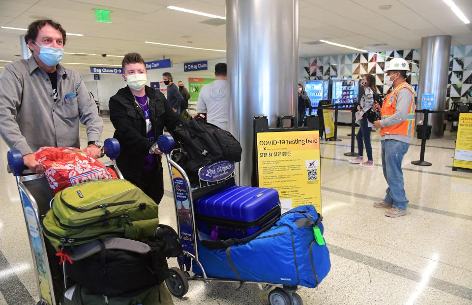 Travellers with their luggage walk past the Covid-19 Testing location at the airport in Los Angeles, California on 23 November 2021 (AFP via Getty Images)