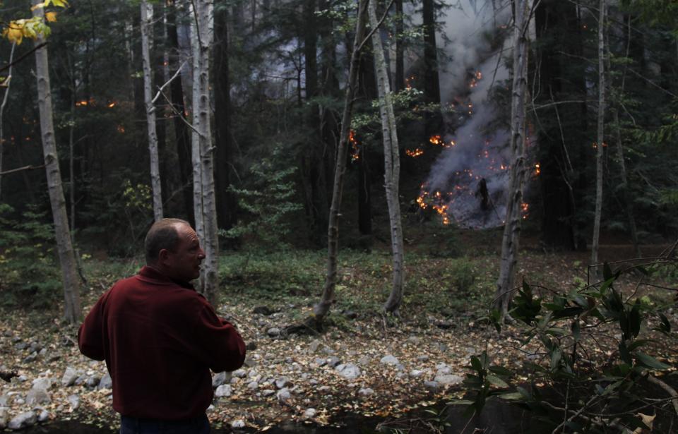 A visitor watches as a wildfire burns along the Big Sur River in Big Sur, California