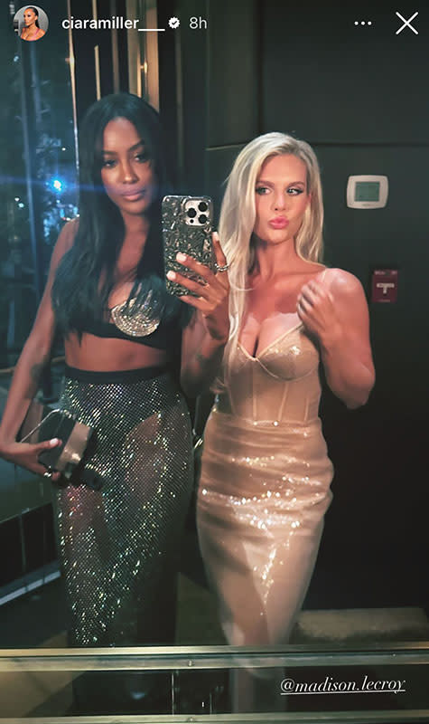 Ciara Miller and Madison LeCroy in cocktail attire pose in front of a mirror for a selfie.