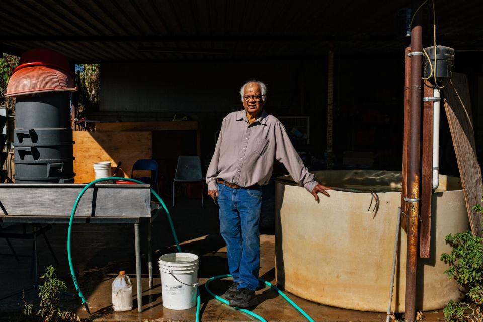 A man stands leaning on a large tub on a farm.