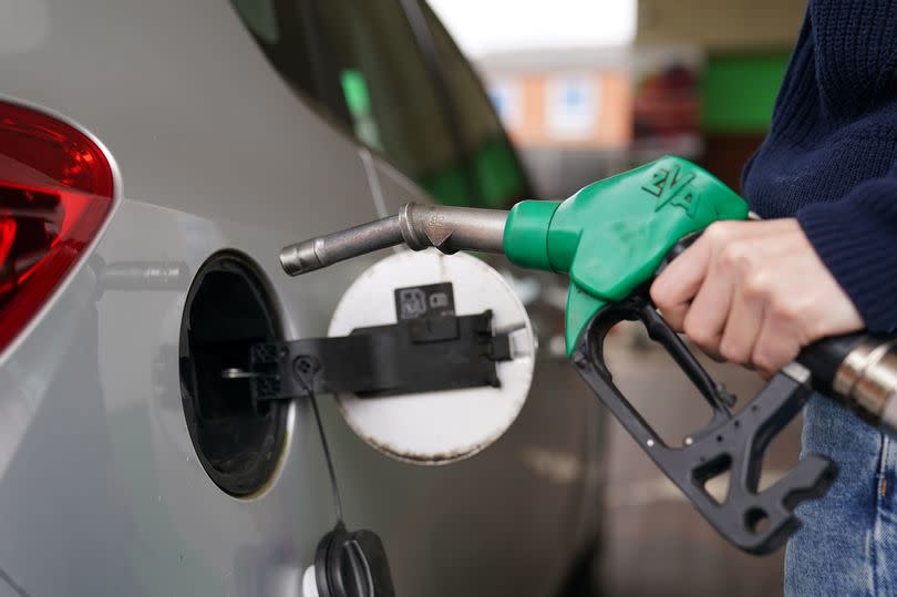 A man fills up his car at the petrol pump. He is holding the pump in his left hand.