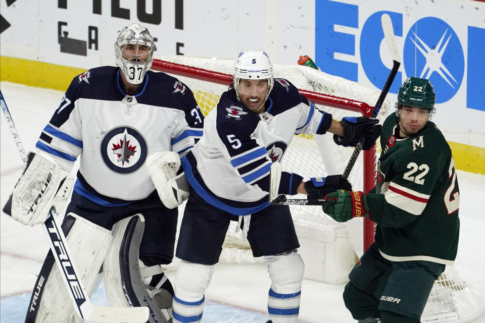 Winnipeg Jets' Brenden Dillon (5) comes to the aid of Jets goalie Connor Hellebuyck (37) as he tries to keep Minnesota Wild's Kevin Fiala (22) at bay in the first period of an NHL hockey game, Friday, Nov. 26, 2021, in St. Paul, Minn. (AP Photo/Jim Mone)