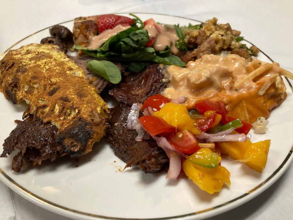 A plate at Made in Brazil in Barre, shown April 22, 2022, displays items including picanha steak, chicken wrapped in bacon, grilled pineapple with cinnamon, chicken stroganoff, tropeiro, mango ceviche and salad with strawberries.