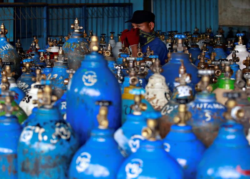 An employee adjusting a scarf on his face walks near oxygen cylinders at a factory amid the coronavirus disease (COVID-19) outbreak in Jakarta