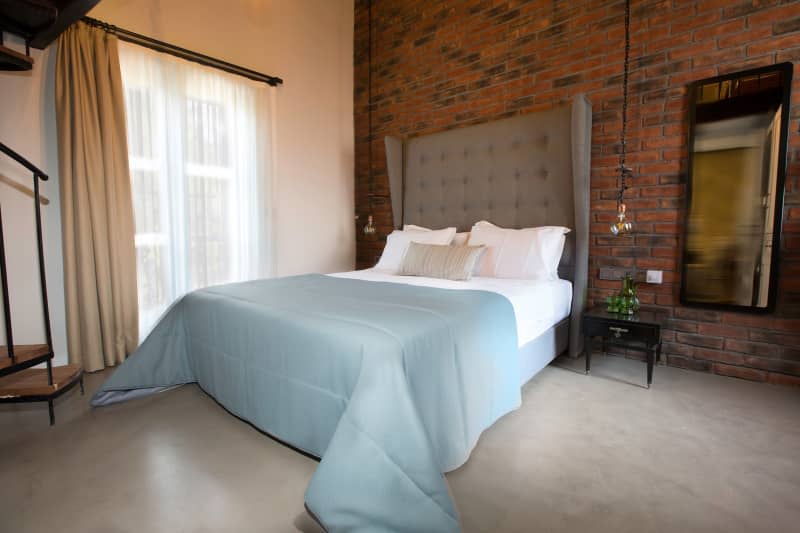 Vintage design hotel bedroom with old decoration, wooden window, light blue bed sheets, white pillows, runner, concrete floor paving and brick wall.