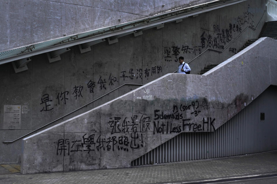 In this Sept. 16, 2019, photo, a man walks down a pedestrian stairway outside the government headquarters which is filled with anti-government graffiti written in English and Chinese, one line in Chinese reads " it is you who teach me peace is useless." As Hong Kong enters its fourth month of steady protests, the city is embracing for another violent weekend prior to the upcoming 70th National Day on Oct. 1. (AP Photo/ Vincent Yu)