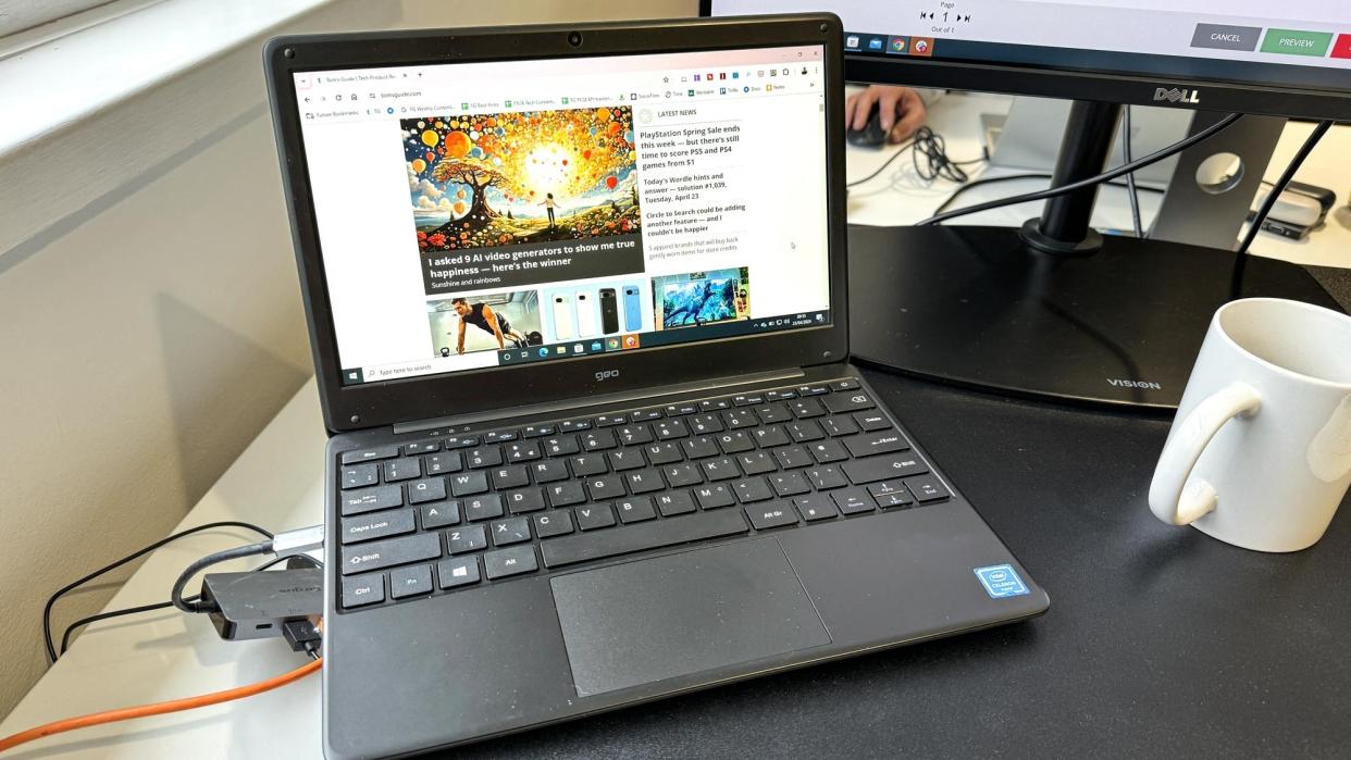  The Geobook 2E budget laptop on a desk in front of an external monitor in a brightly lit office. 